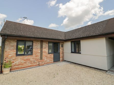 An exterior view of a single story house with a gravel driveway and a wooden door at Garden Cottage in Upton Upon Severn