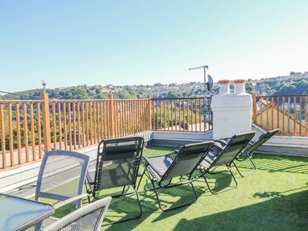 A rooftop terrace with chairs and a table overlooking houses and green hills at Penmar in Looe