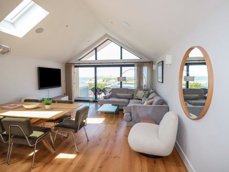A living room with a dining table and chairs a gray sofa a white armchair and a large window with sea view at Porth Cove in Porth
