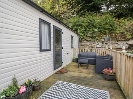 An outdoor deck with black patio furniture and potted plants next to a white building at Burlees Nest in Brigham near Great Broughton Cockermouth