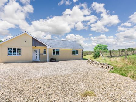 A single story house with a gravel driveway and a fenced grass area at Cae Berllan in Mynytho near Pwllheli