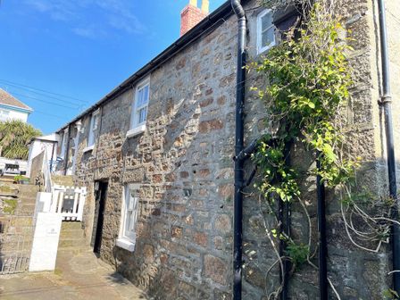 An exterior view of a stone cottage with white framed windows and a plant growing along a downpipe at The Little Net Loft in Mousehole near Penzance