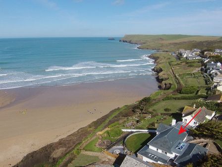 A coastal landscape with a beach and waves next to houses on a cliff at The White House in Polzeath