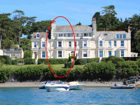 A large cream-colored building with multiple windows and chimneys by a waterfront with boats at 4 The Terrace in Rock