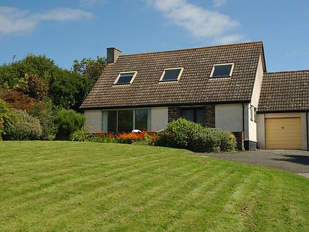 A house with three roof windows and a yellow garage door with a lawn and bushes at Rosevallen in Daymer Bay