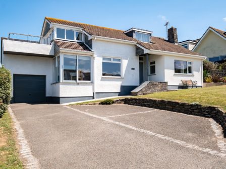 A driveway with marked parking spaces leading to a white house with a garage and front garden at Little Belz in Polzeath