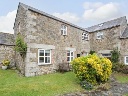A stone house with multiple windows a wooden bench and bushes in the garden at The Granary in Rock