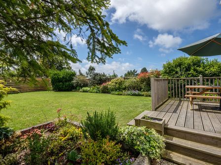 A garden with grass lawn surrounded by plants and shrubs next to a wooden deck with a picnic table and umbrella at Cogenhoe in Rock