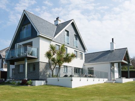 A modern house with a glass balcony and a patio on a grassy lawn at Ragleighs in Daymer Bay