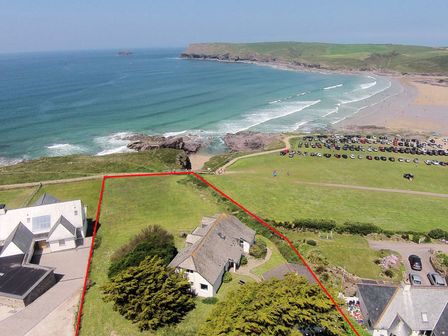A coastal property with a house and green yard near a beach with parked cars at Gullsway Kittiwake in Polzeath
