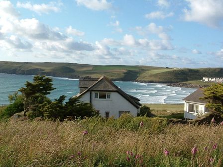 A coastal scene with houses near the shore overlooking the ocean and grassy hills in Polzeath