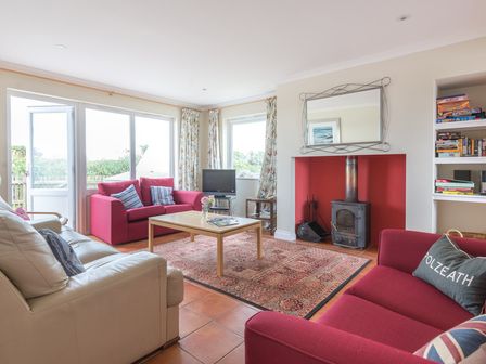 A living room with red and white sofas a wooden coffee table a rug and a fireplace at Kirra in Polzeath