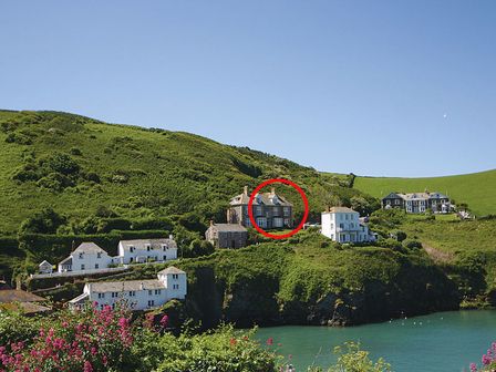 Houses on a green hillside above a body of water with flowers in the foreground at Folly 2 in Port Isaac