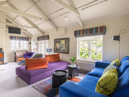 A living room with colorful sofas and armchairs by windows and a fireplace at Crow's Nest in Port Isaac