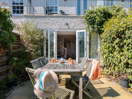 An outdoor patio with a wooden table and chairs near a house with open doors at Lowenna Manor 4 Rock