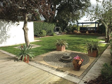 A garden with grass lawn trees potted plants a circular stone feature and a wooden swing at Belmont Rock