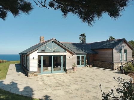 A house with large windows and a tiled patio by the ocean at Ossco in Polzeath
