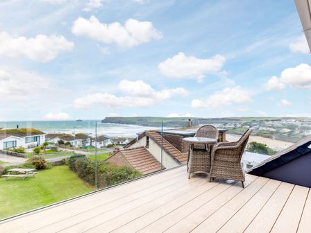 A balcony with two wicker chairs and a small table overlooking houses and the coastline at Atlantis in Polzeath
