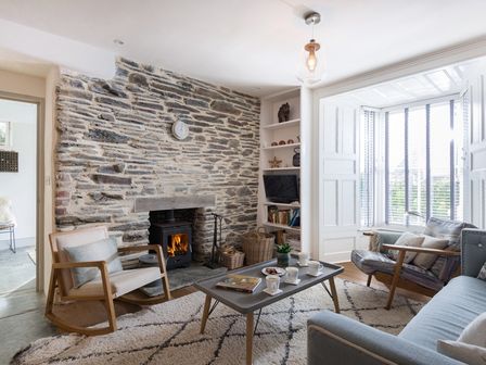 A living room with a stone wall fireplace wooden rocking chair coffee table and sofa at Albany in Port Isaac