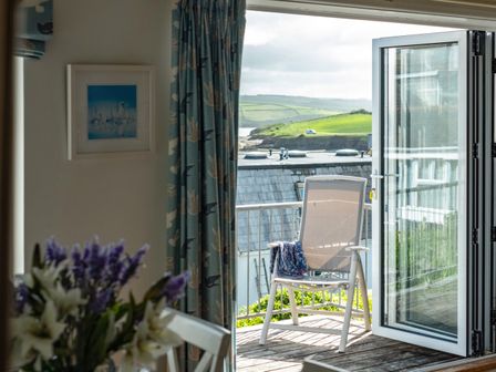 A room with flowers on a table and an open door leading to a balcony with a chair and a view of green hills at Slipway 12 Rock