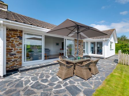 A patio with a glass table and six wicker chairs under a large umbrella outside a house at Tremay in Rock