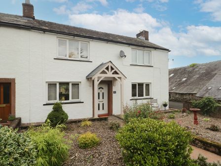 A white cottage house with a wooden porch and garden beds with bushes at 3 Springfort Cottages in Newton Reigny near Penrith