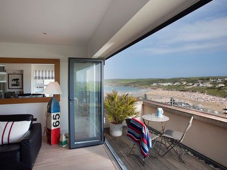 A balcony with two chairs a small table a towel and a potted plant overlooking a beach and sea at Kellan in Polzeath