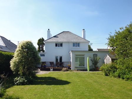 A two-story white house with a wooden deck and outdoor furniture in a garden at The Moorings in Rock