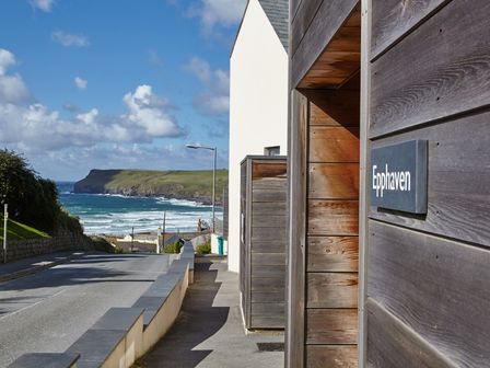 A street with wooden wall and a sign reading Epphaven with a view of the ocean and cliffs in Polzeath