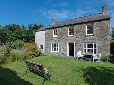 A stone house with white window frames and a garden bench on the lawn at Conifers Rock