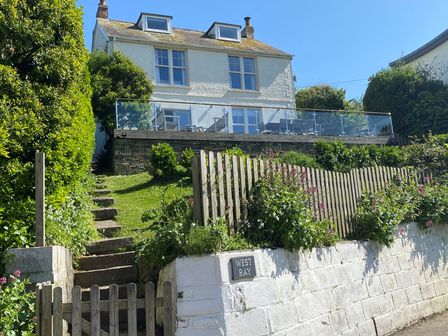 A two-story house with skylights with a garden and steps leading up behind a wooden gate at Westray House in Polzeath