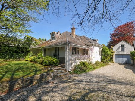 A detached house with a covered porch garden plants and a detached garage with a gravel driveway at Sandy Lodge Rock