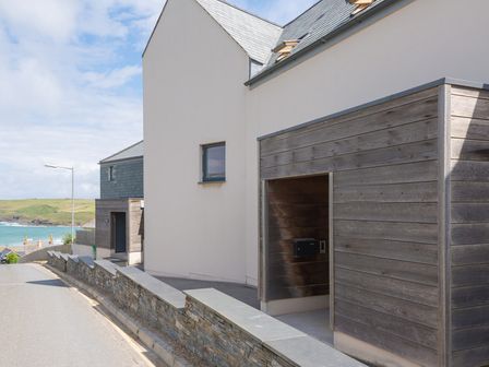 A coastal street with modern houses and a stone wall near the sea at Rainer Rocks in Polzeath