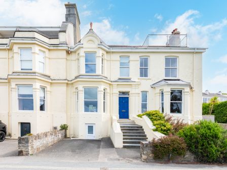 A cream colored semi detached house with a blue front door and steps leading up surrounded by bushes and a driveway at The Terrace 2 in Rock
