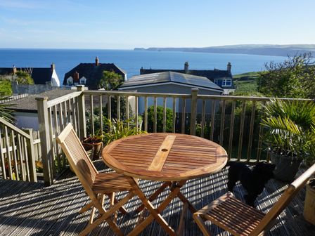 A wooden deck with a round table and two chairs overlooking houses and the sea at The Porthole in Port Isaac