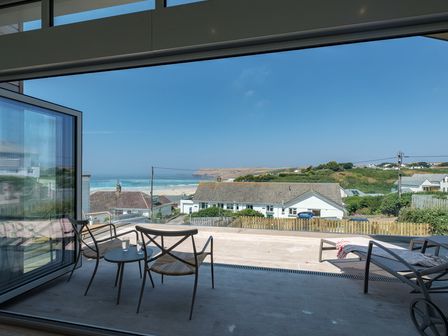 A patio with chairs and a table overlooking houses and a beach at Point Break in Polzeath