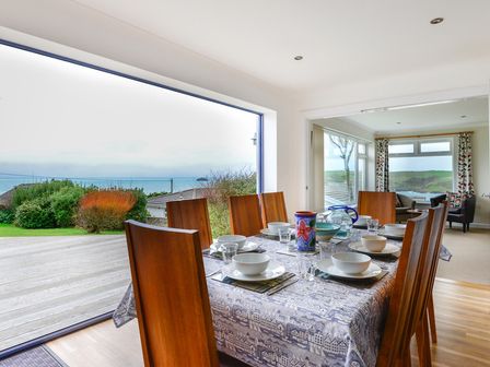 A dining table set with bowls and glasses next to large window showing garden and water view at Sea Mist in Polzeath