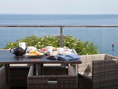 A table with breakfast items and a magazine on a balcony overlooking the sea at The Crows Nest in Port Isaac