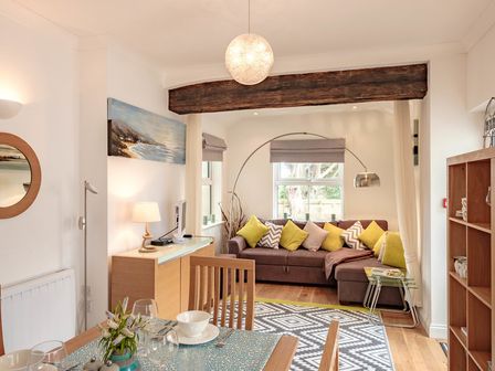 A living room with a brown sectional sofa with yellow and patterned cushions a dining table with place settings and a blue patterned tablecloth at St Martins Apartment in Rock