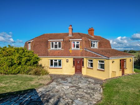 A two-story house with yellow walls and brown roof surrounded by grass and bushes at Trevan House Lundy Polzeath
