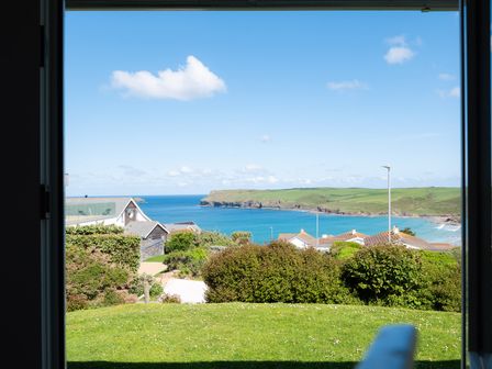 View of a coastline with houses trees and grass from inside a building at Windyhill Polzeath