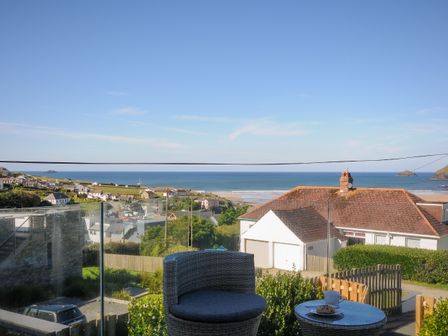 A balcony with a round table and chair overlooking houses and the ocean at Drishti in Polzeath