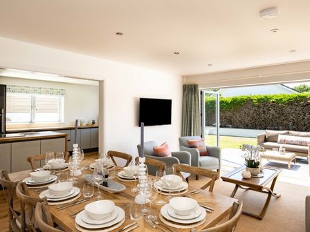 A dining area with a set table of plates glasses and cutlery next to a living area with chairs a coffee table and a television and an open patio with outdoor seating at Artemis Rock