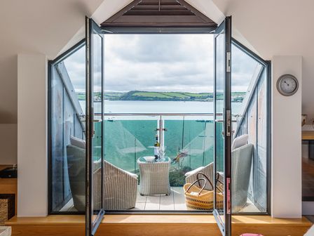 A balcony with wicker chairs a small table and a basket overlooking a body of water and distant hills at Upper Deck in Rock