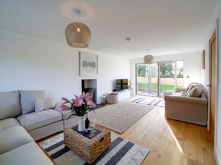 A living room with sofas a coffee table with flowers a TV and glass doors leading outside at Elmwood in Port Isaac