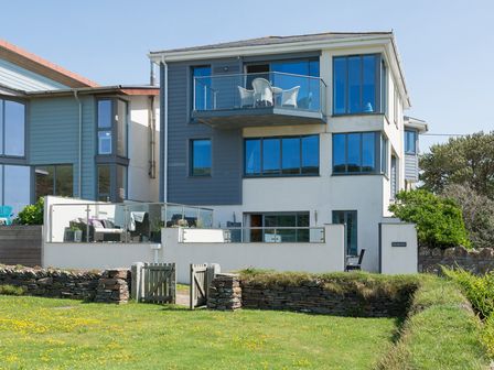 A modern three-story house with balconies and a garden with a wooden gate at Egloskerry in New Polzeath