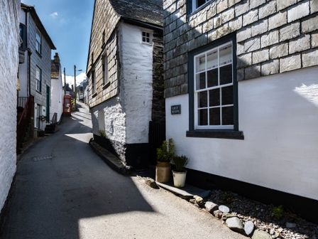 A narrow street with white stone houses and a red telephone box at Grey Roofs in Port Isaac