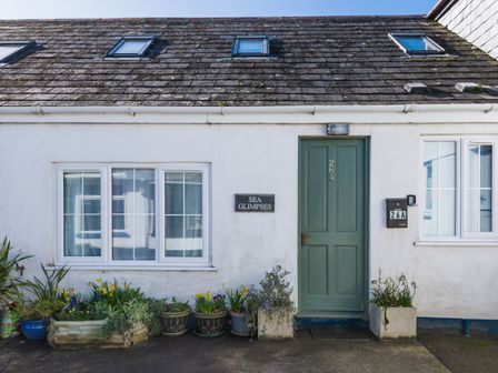 The front exterior of a white house with a green door numbered 26A and flower pots below the windows at Sea Glimpses in Port Isaac
