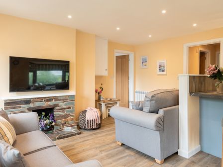A living room with two gray sofas a wall-mounted TV and a small table with flowers at Brookside in Polzeath
