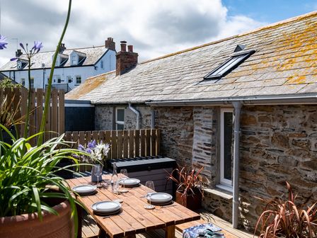 An outdoor patio with a wooden dining table set with plates and glasses surrounded by plants and a stone building at Mino Cottage in Port Isaac